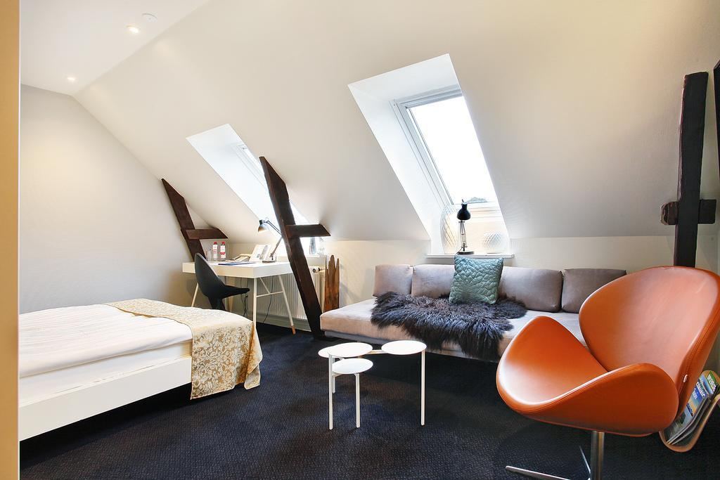 Queen size-værelse med seng, skrivebord og orange lænestol ved tagvinduet